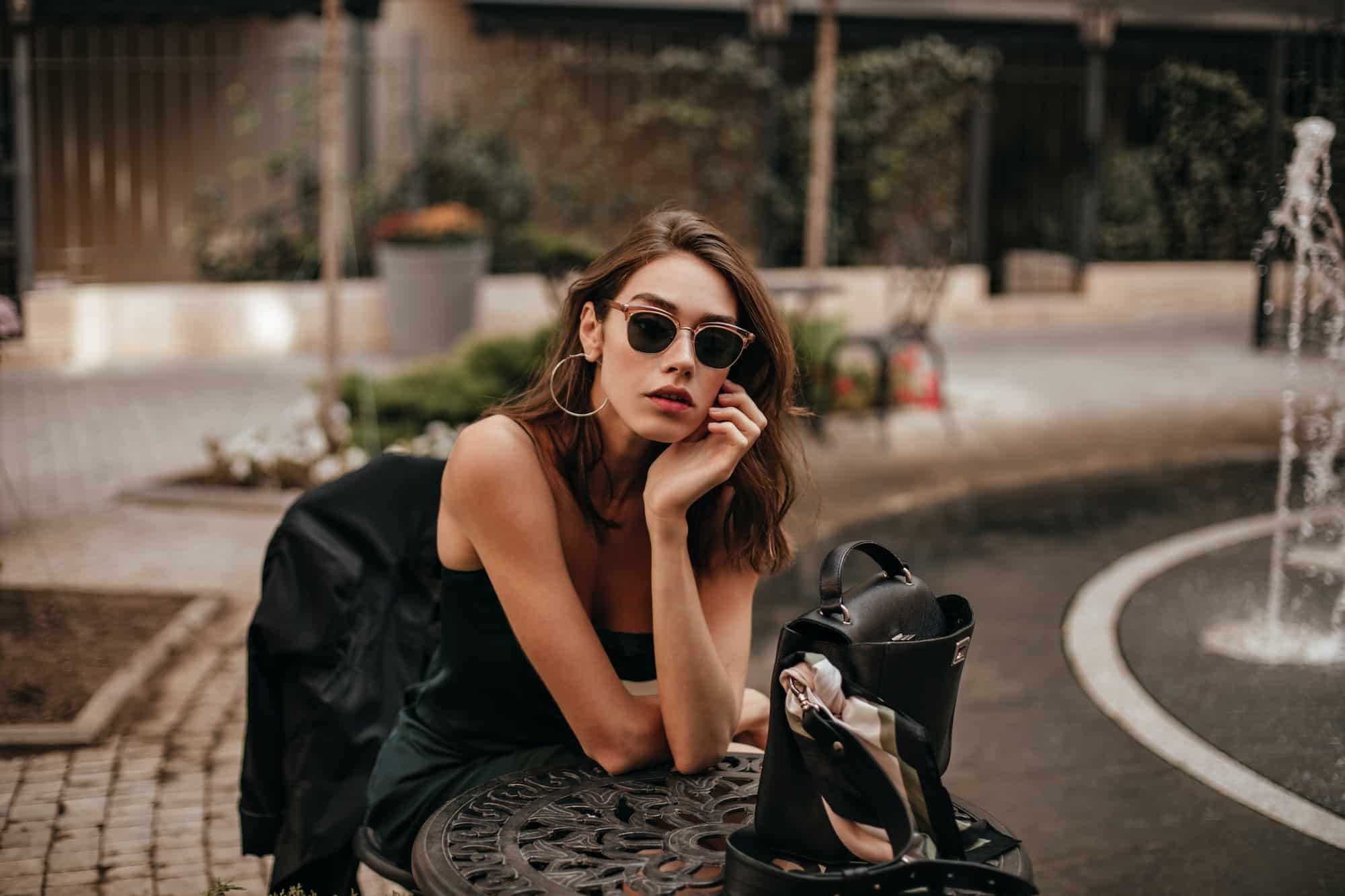Pretty young girl with dark wavy hairstyle, red lips and black sunglasses, wearing slip green dress